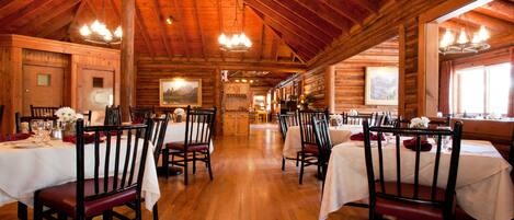 A wooden interior with tables set for dining, wooden beams on the ceiling, and a chandelier.