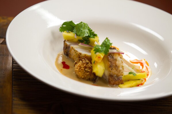 A white plate with a dish of food, including meat, fruit, and a sauce.