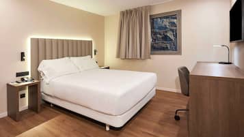 Une chambre d’hôtel avec un lit, une table de chevet, une lampe, un bureau, une chaise et un tableau au mur.