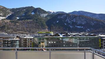 A modern hotel with a glass facade, located in a mountainous area with snow-capped peaks in the background.