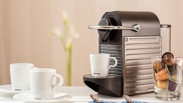Eine Nespresso-Kaffeemaschine mit zwei Tassen und einem Glas auf einem Tisch.