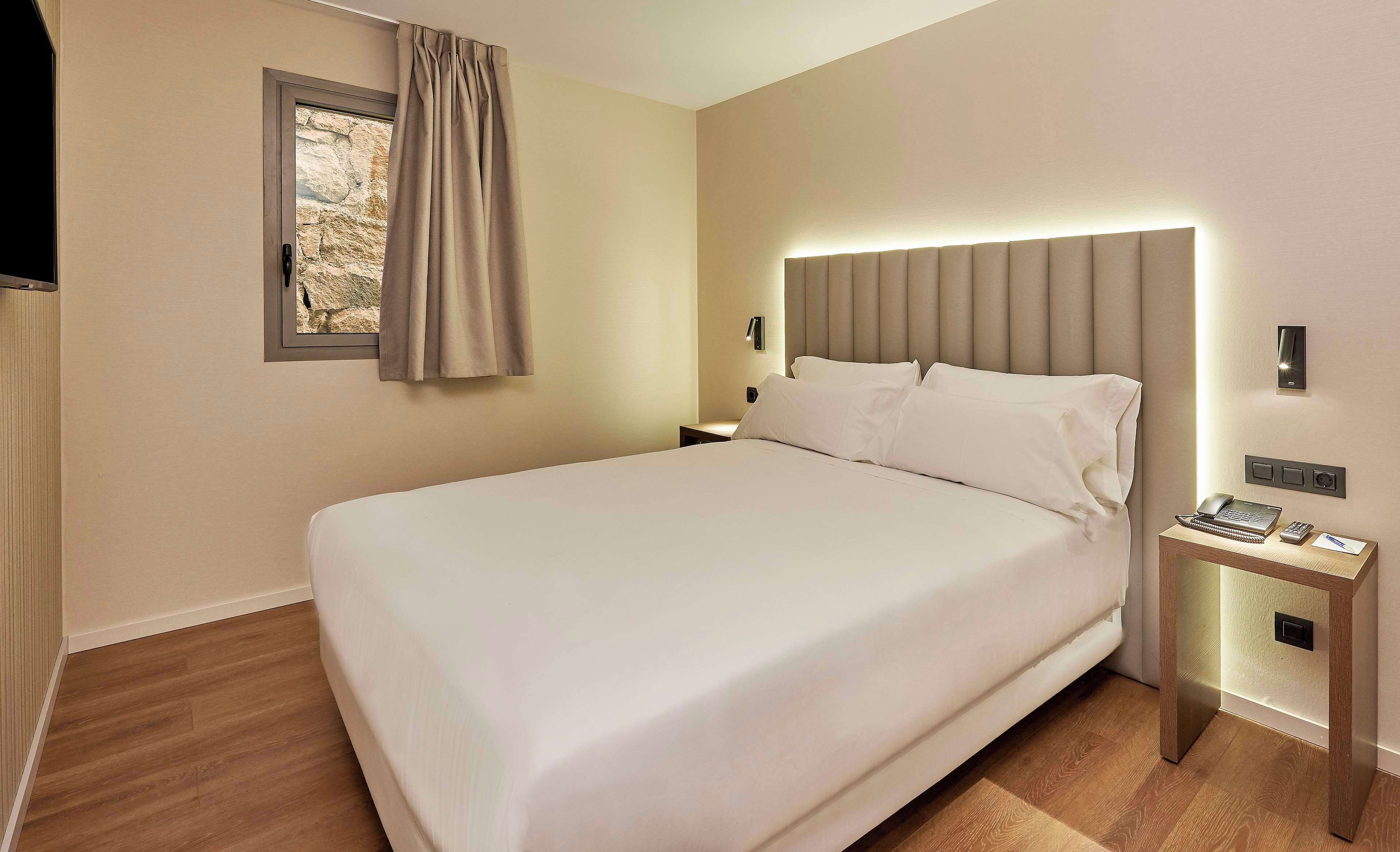 A neatly made bed in a hotel room with a headboard, bedside tables, and a wall-mounted phone.