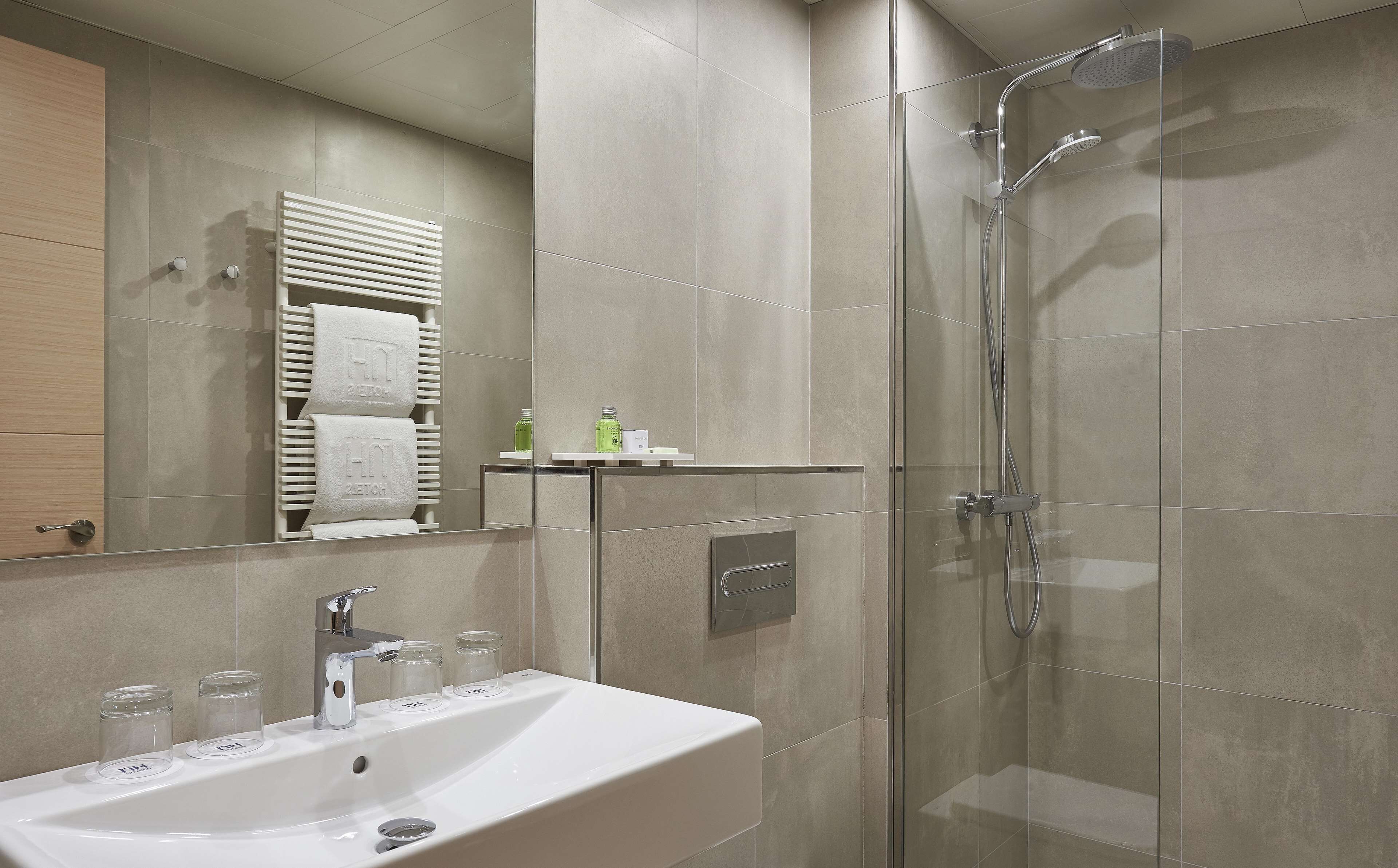 Une salle de bain moderne avec une douche à parois de verre, un lavabo blanc agrémenté de deux pots en verre et un porte-serviettes avec deux serviettes.
