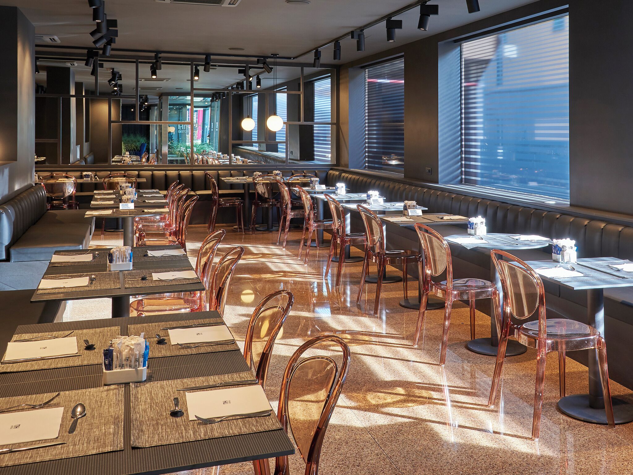 Un restaurante espacioso con mesas y sillas altas, ventanas amplias y una decoración de diseño moderno.