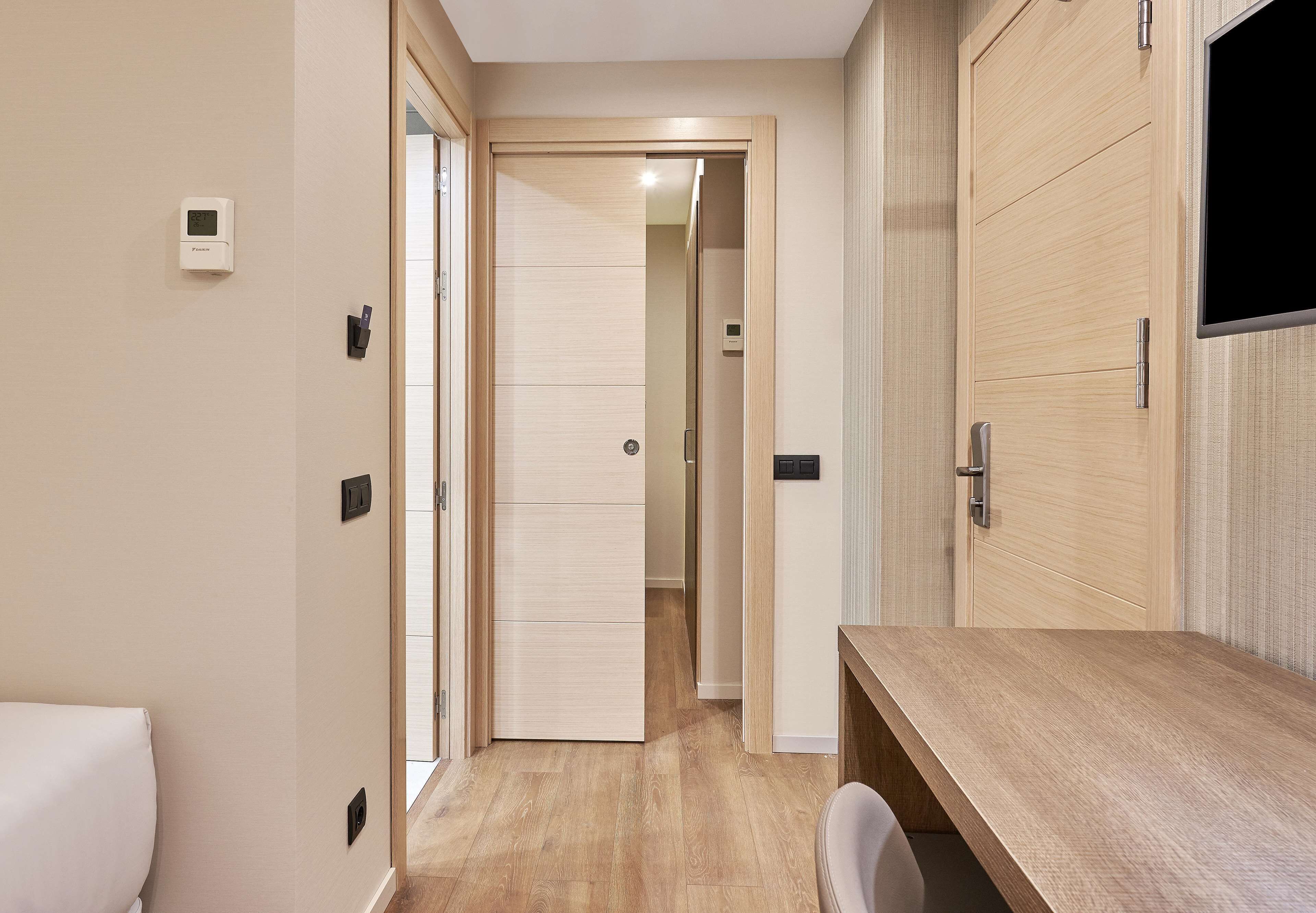Un pasillo con suelo de madera, una puerta blanca y un escritorio de madera con una silla.