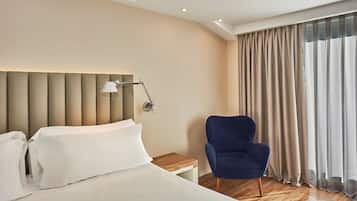 Ein Hotelzimmer mit Bett, Nachttisch, Lampe, Stuhl und einem großen Fenster mit Vorhängen.