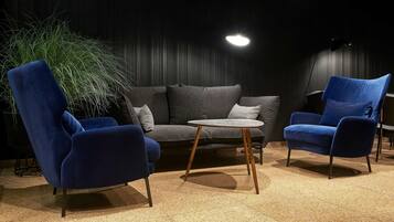 Una sala de estar moderna con un sofá gris, dos sillones azules, una mesita redonda y una planta grande en maceta.