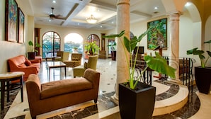 Um hall amplo com um sofá marrom, poltronas, mesa de centro e plantas em vasos.