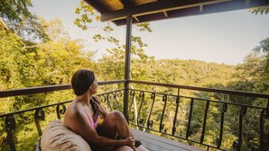 Uma mulher sentada em um deck de madeira com vista para uma paisagem arborizada.