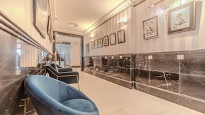 Um hall de hotel com piso de mármore, balcão de recepção e obras de arte emolduradas nas paredes.