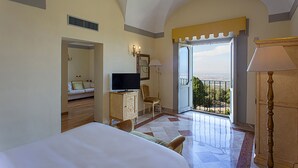 A hotel room with a bed, a television, a chair, a desk, a lamp, and a balcony with a view. - Villa Tuscolana (Frascati)