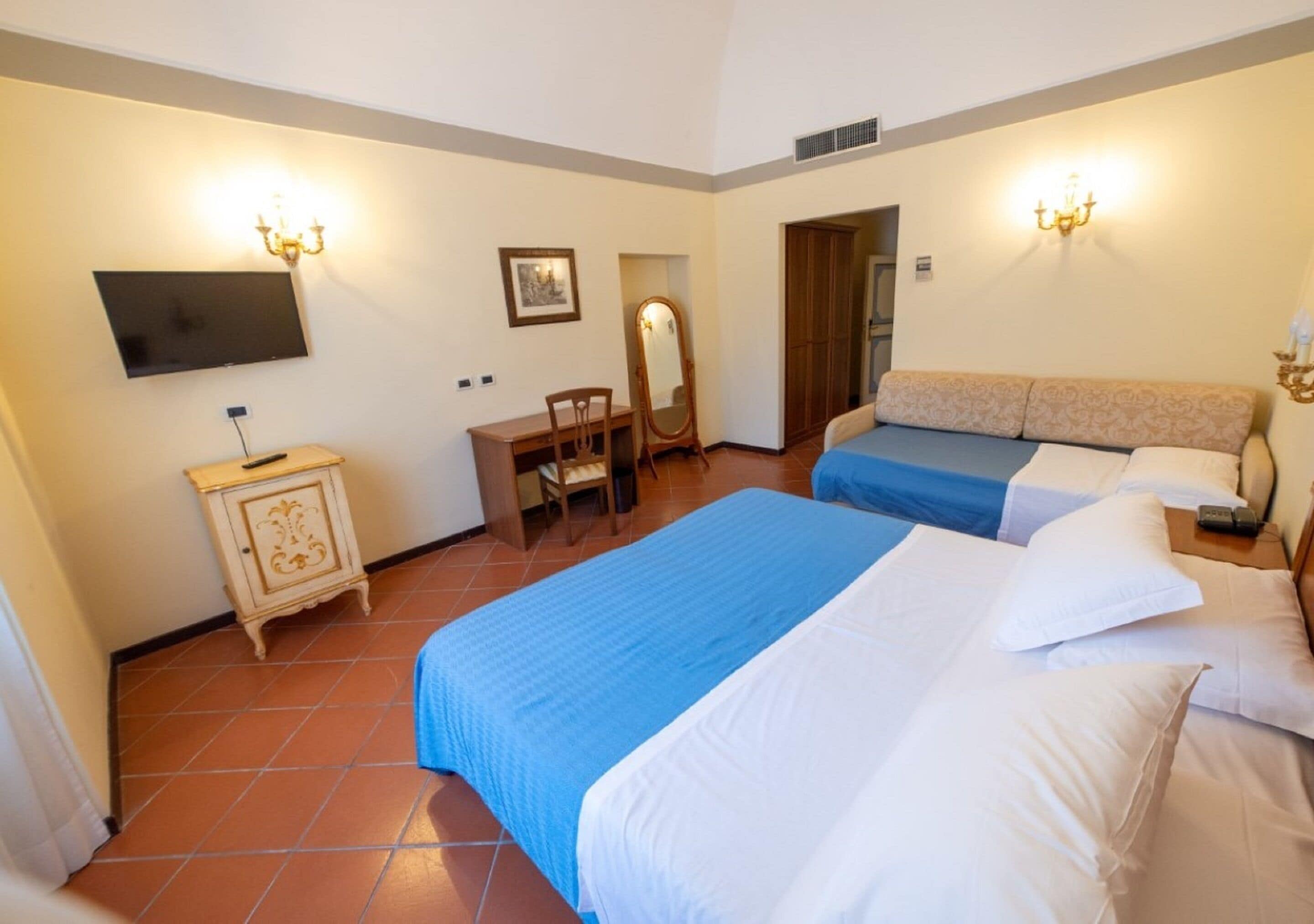 A hotel room with two beds, a desk, a chair, a wardrobe, and a television.
