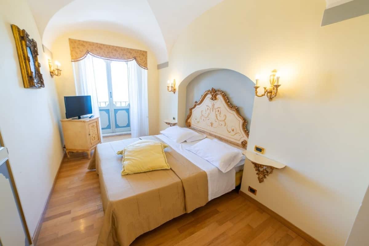 Een slaapkamer met een bed, een televisie, een houten kast en uitzicht op een balkon.