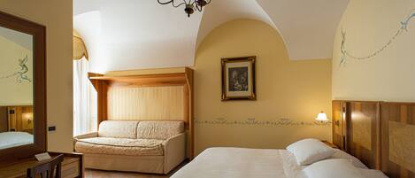 Une chambre d’hôtel avec un lit, un bureau, une chaise, un lustre et un tableau au mur.