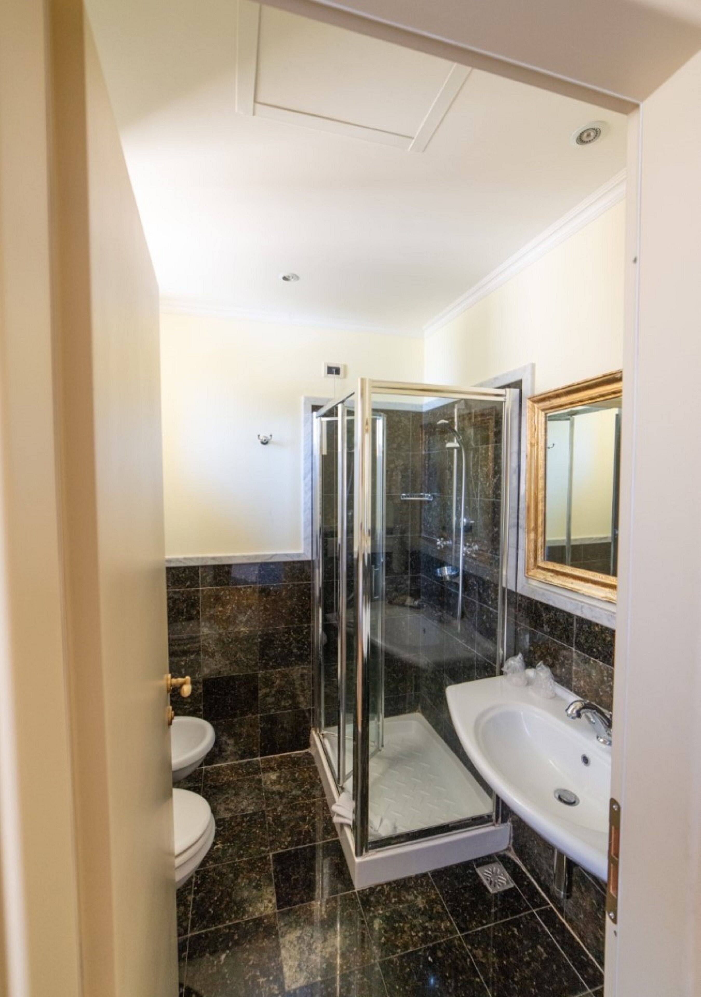 A bathroom with a glass-enclosed shower, two sinks, and a toilet.