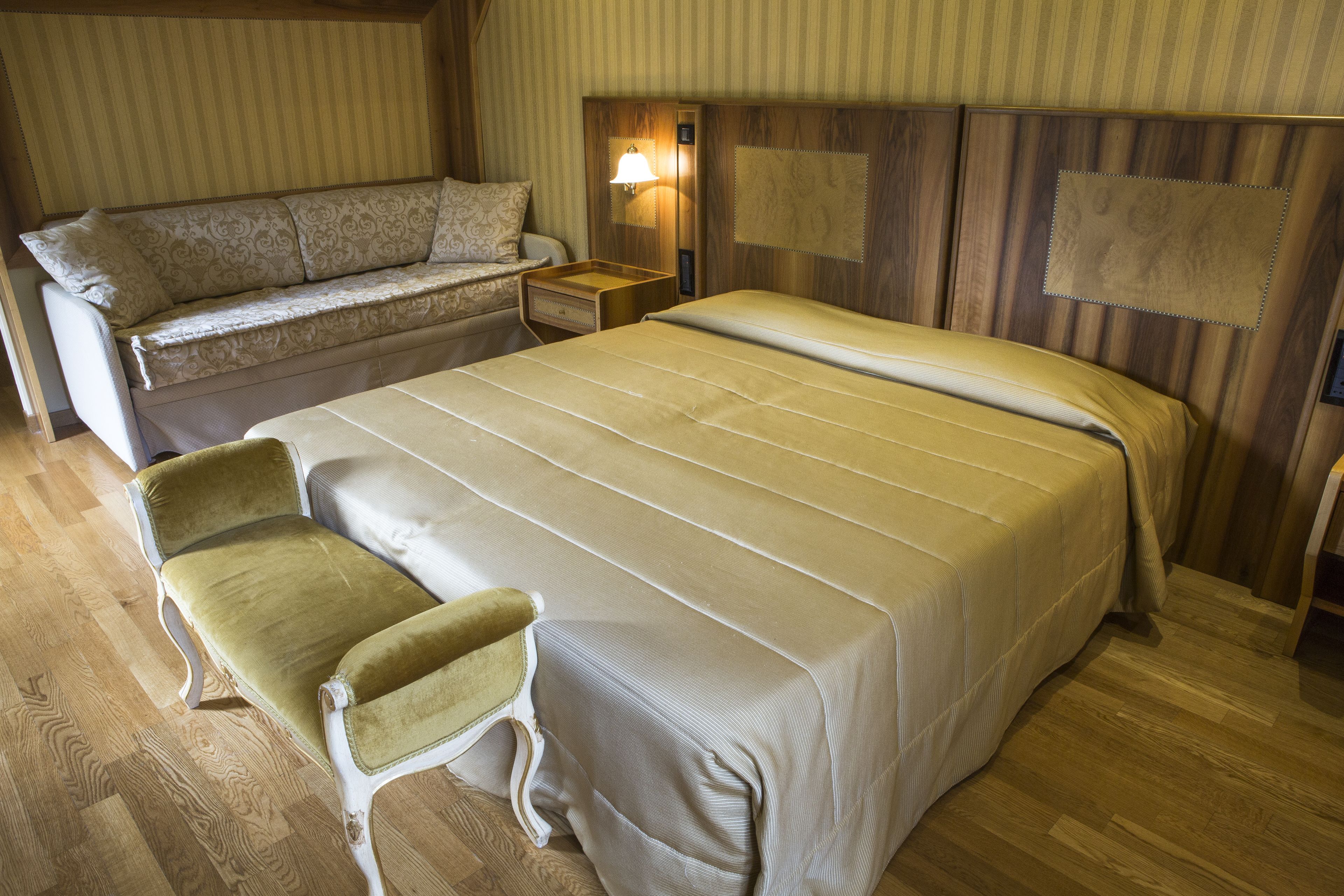 A hotel room with a bed, a sofa, a chair, a nightstand, and a wall-mounted lamp.