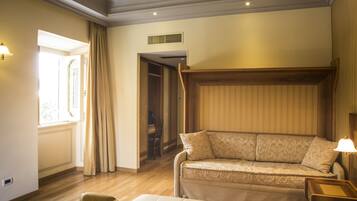 Une chambre d’hôtel avec un canapé, un fauteuil, une lampe et une fenêtre avec des rideaux.