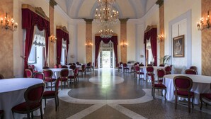 A formal dining room with round tables, red upholstered chairs, and a central chandelier. - Villa Tuscolana (Frascati)