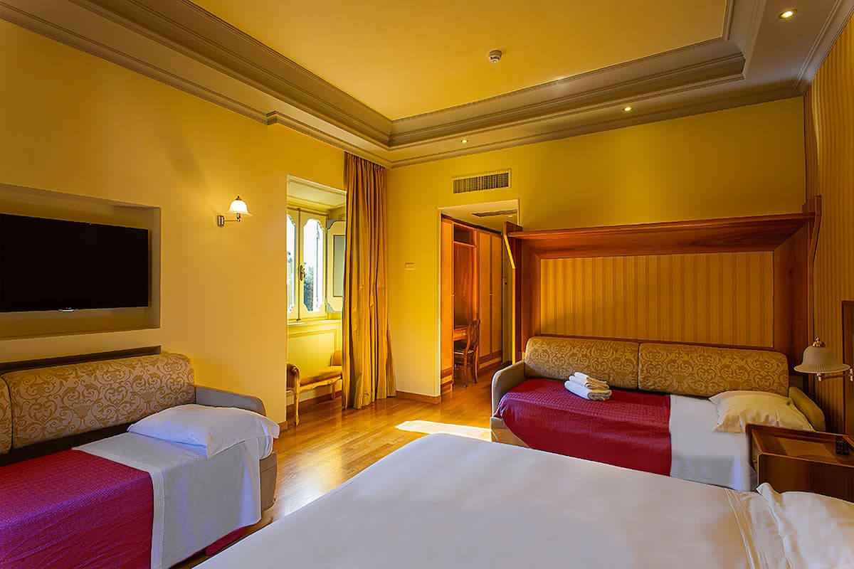 Een hotelkamer met twee enkele bedden, een flatscreen televisie, een houten hoofdbord en een klein tafeltje met een lamp.