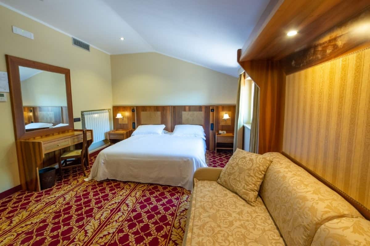 Een hotelkamer met twee bedden, een bank, een houten hoofdeinde, een spiegel, een bureau en een kamerkleed met een patroon.