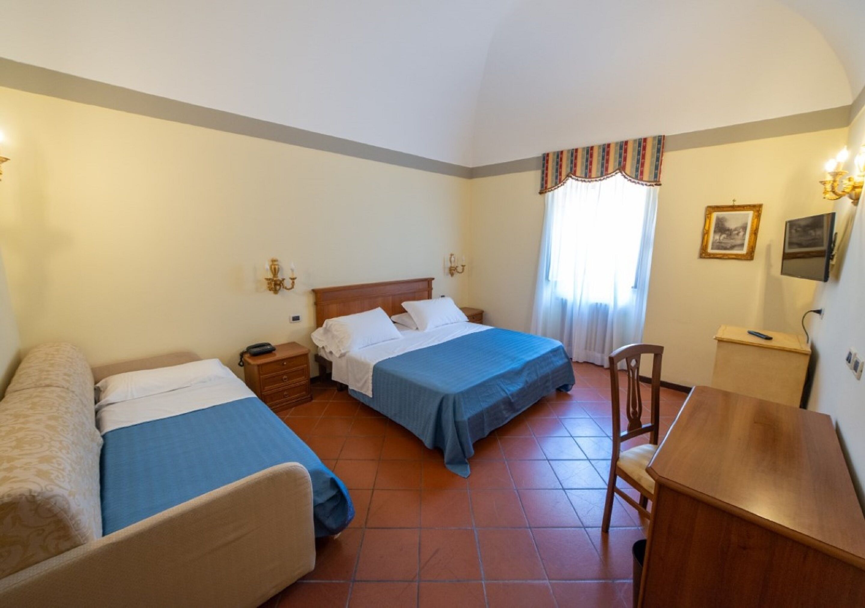 A hotel room with two single beds, a wooden desk, a chair, a nightstand, and a small cabinet.