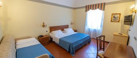 A hotel room with two single beds, a wooden desk, a chair, a nightstand, and a small cabinet.