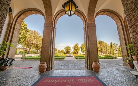 An arched entrance with a red carpet, a hanging lantern, and a view of a garden with a fountain.