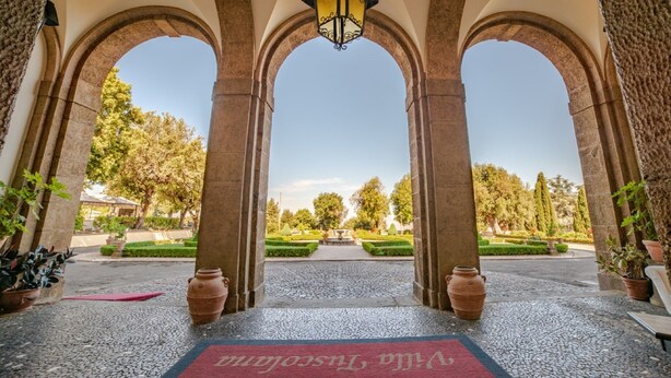 An arched entrance with a red carpet, a hanging lantern, and a view of a garden with a fountain. - Villa Tuscolana (Frascati)
