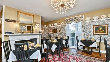 Uma sala de jantar com um candelabro, uma lareira e um tapete vermelho estampado.