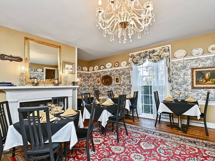 Uma sala de jantar com um candelabro, uma lareira e um tapete vermelho estampado.