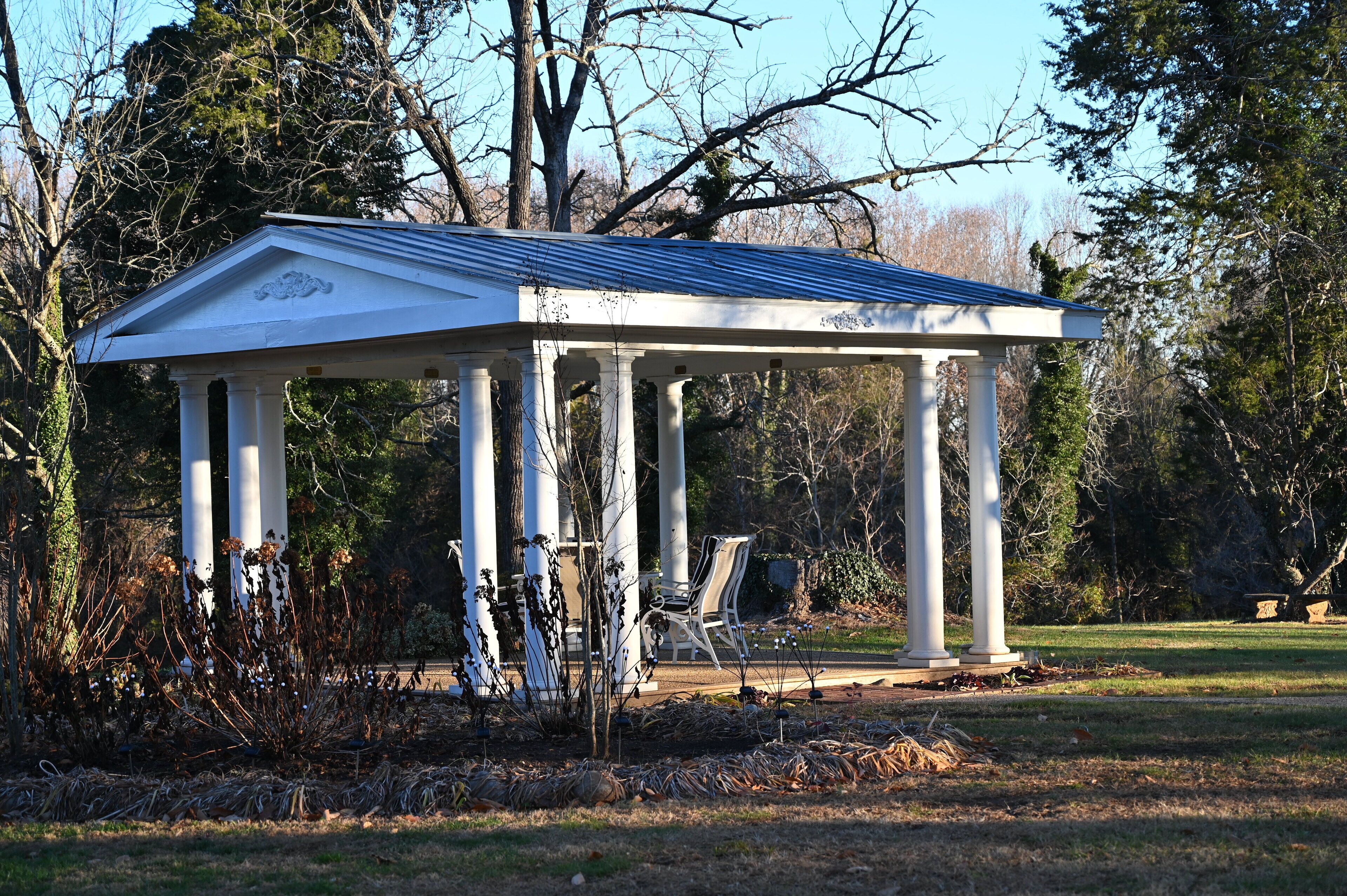 Un gazebo bianco con colonne, circondato da alberi e arbusti.
