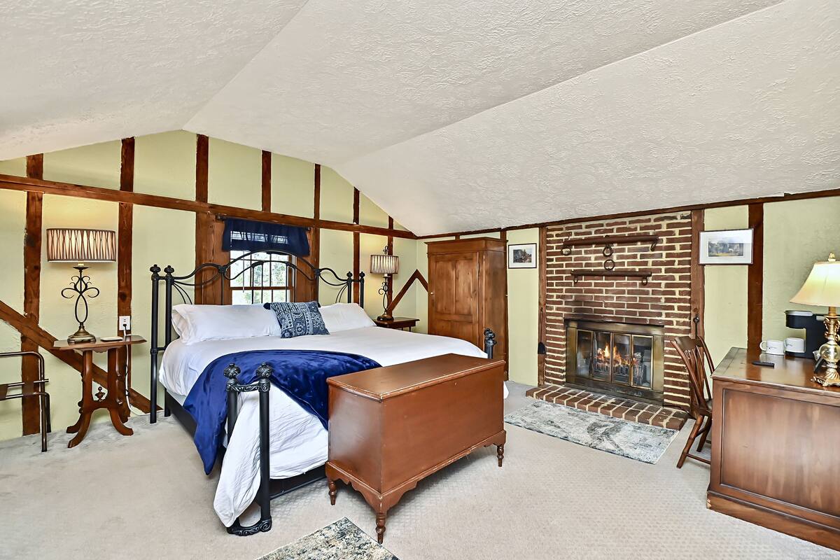 Un dormitorio con una cama grande, un aparador de madera, una chimenea y una ventana con vistas.