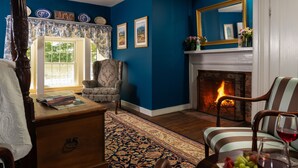 Una sala de estar acogedora con chimenea, un tapete estampado y una mesa de comedor con frutas y copas de vino.