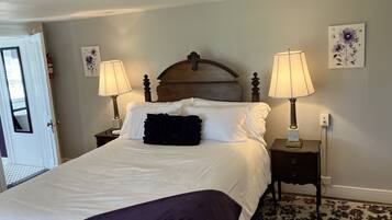 A neatly made bed with white linens and a dark throw blanket, flanked by two bedside tables with lamps, in a room with a patterned carpet and light-colored walls.
