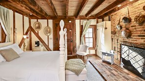 Una habitación rústica con una cama, una silla, una mesita y una chimenea.