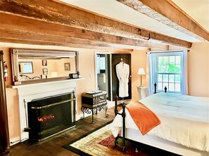 A hotel room with a fireplace, a bed with an orange throw, a large window with a view, and a robe hanging on the door. - Prospect Hill Inn & Restaurant (Louisa)