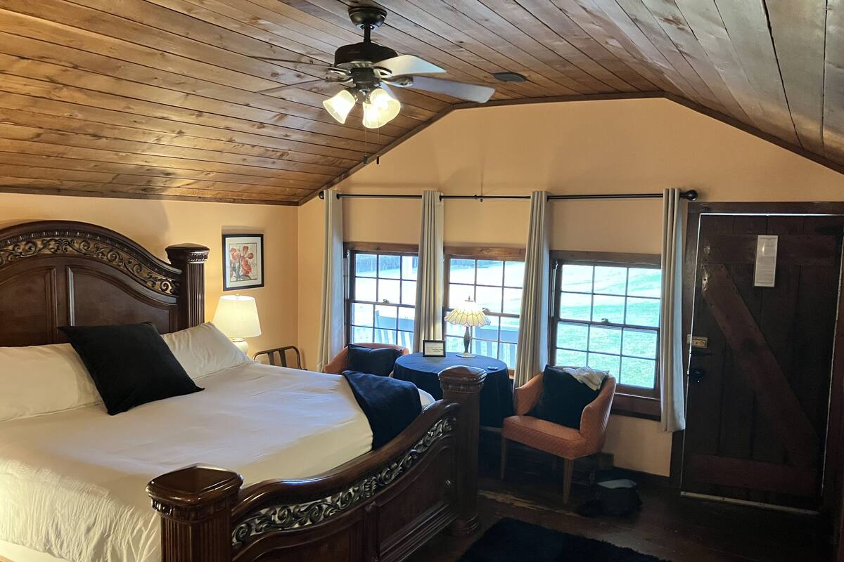 Un dormitorio con techo de madera, una cama grande, un escritorio y una silla junto a una ventana con vistas.