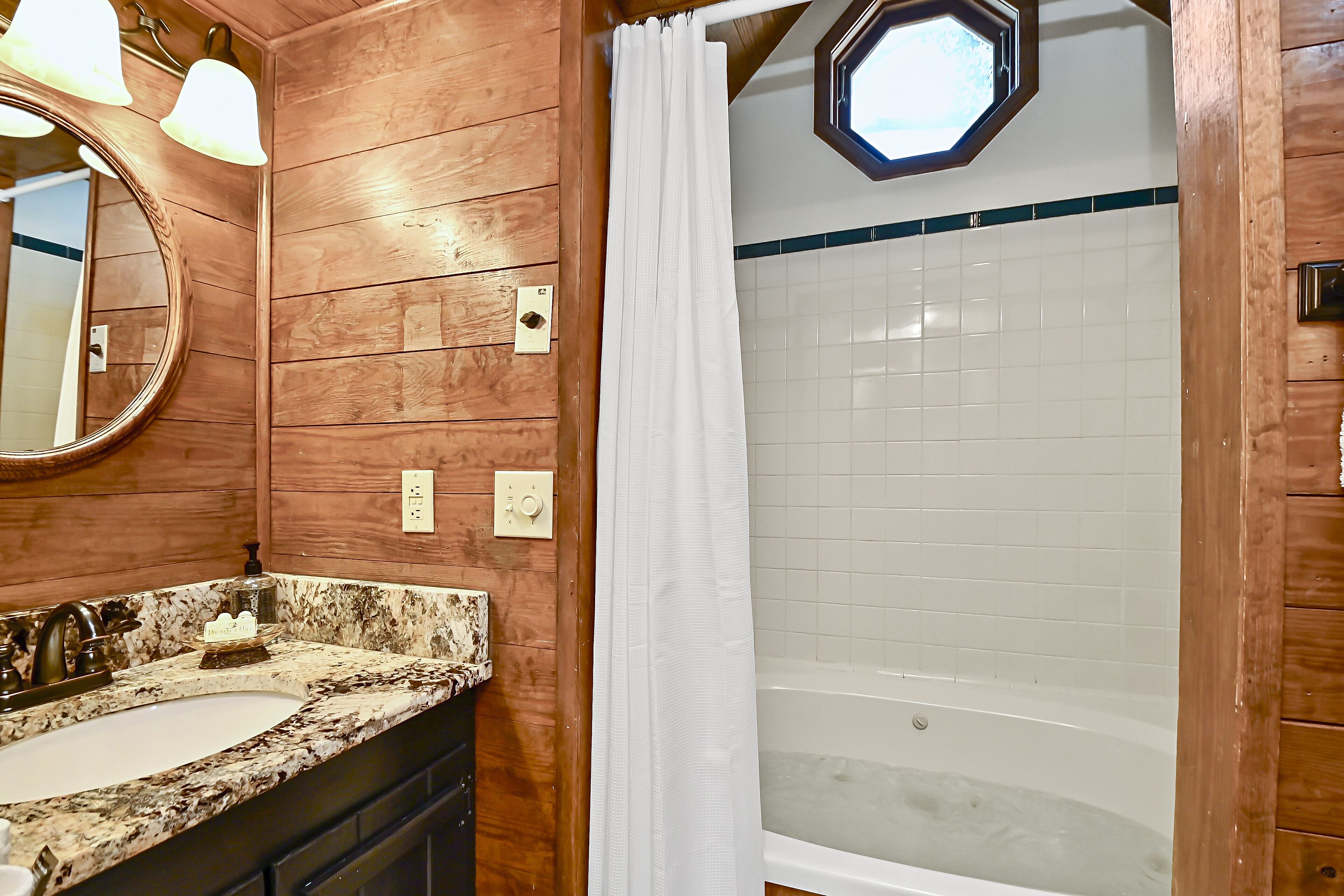 A bathroom with a wooden vanity, a large mirror, a bathtub, and a shower curtain.