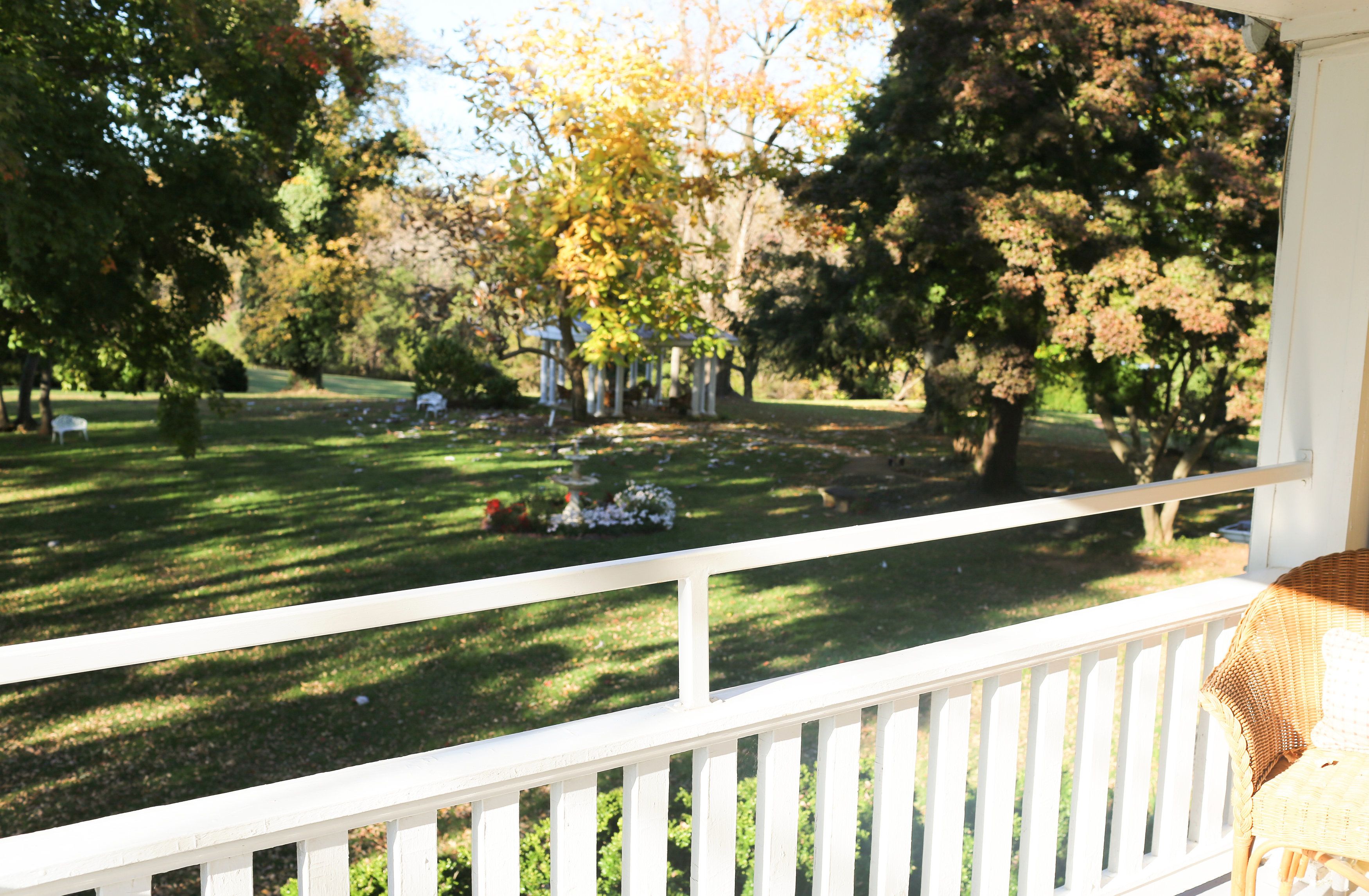 A porch with a white railing overlooking a well-maintained lawn with trees and a gazebo.