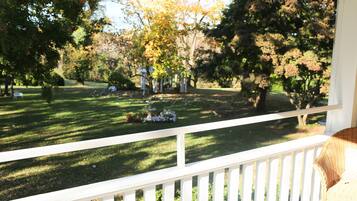 A porch with a white railing overlooking a well-maintained lawn with trees and a gazebo.