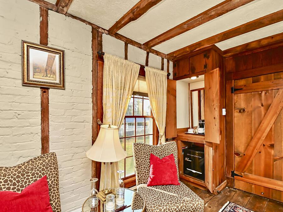 A rustic interior with exposed wooden beams, a fireplace, and a patterned armchair with red cushions.