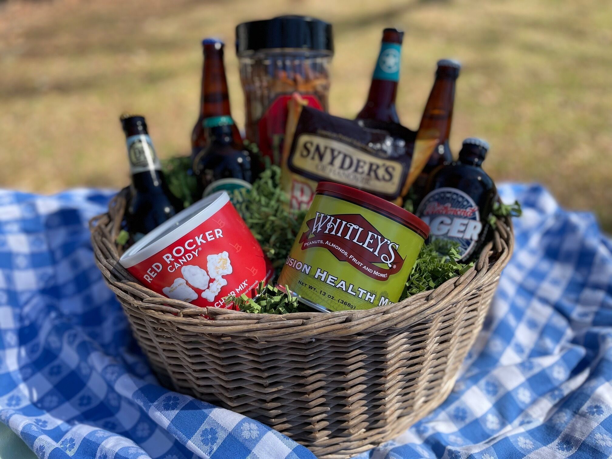 A wicker basket filled with various food items and beverages, placed on a blue and white checkered cloth.
