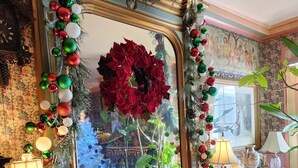 Une pièce avec un grand miroir, des décorations de Noël, une table recouverte d’une nappe rouge et deux lampes.