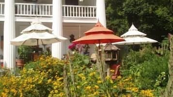 A white building with a balcony, surrounded by yellow flowers and red and white umbrellas.