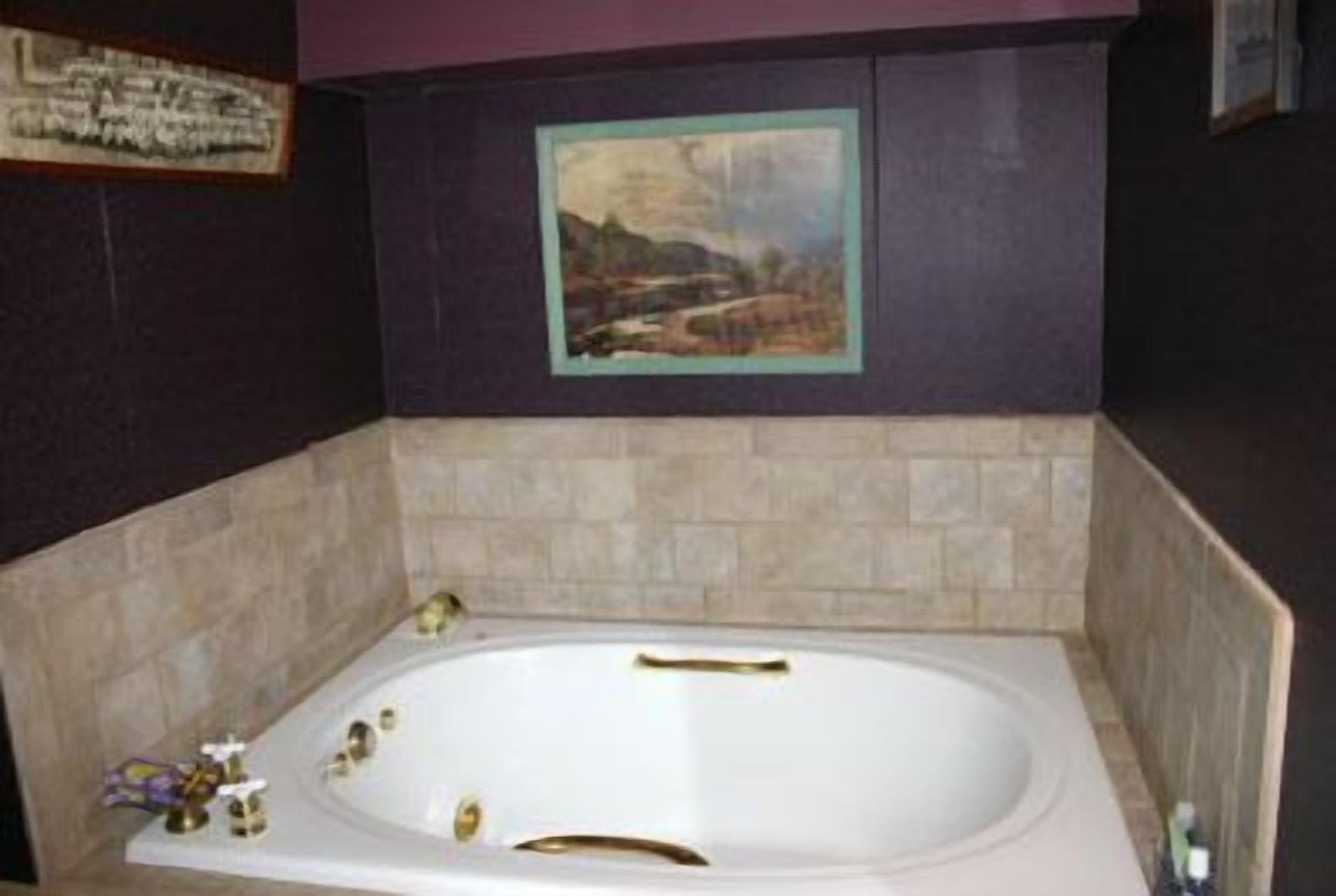 A bathroom with a large bathtub, beige tiles, and a framed painting on the wall.