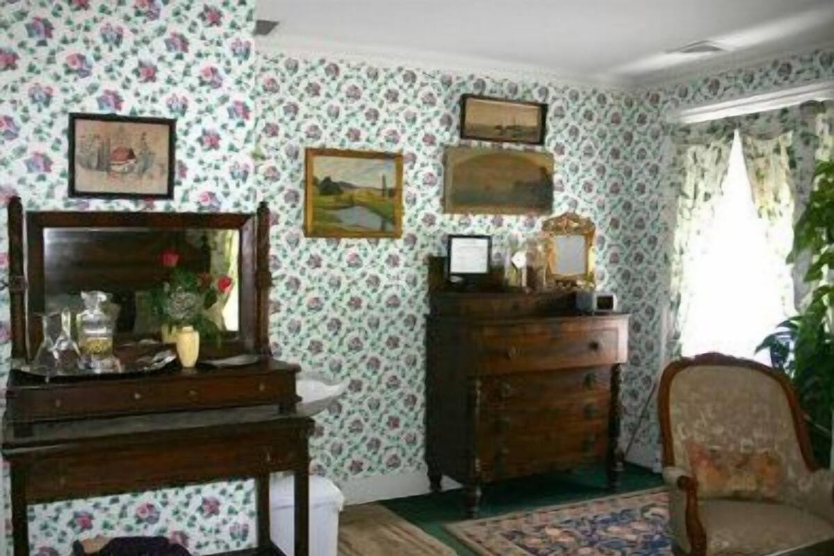 Ein Zimmer mit blumigem Wandpapier, einem Holzschrank, einem Spiegel und einem Stuhl.