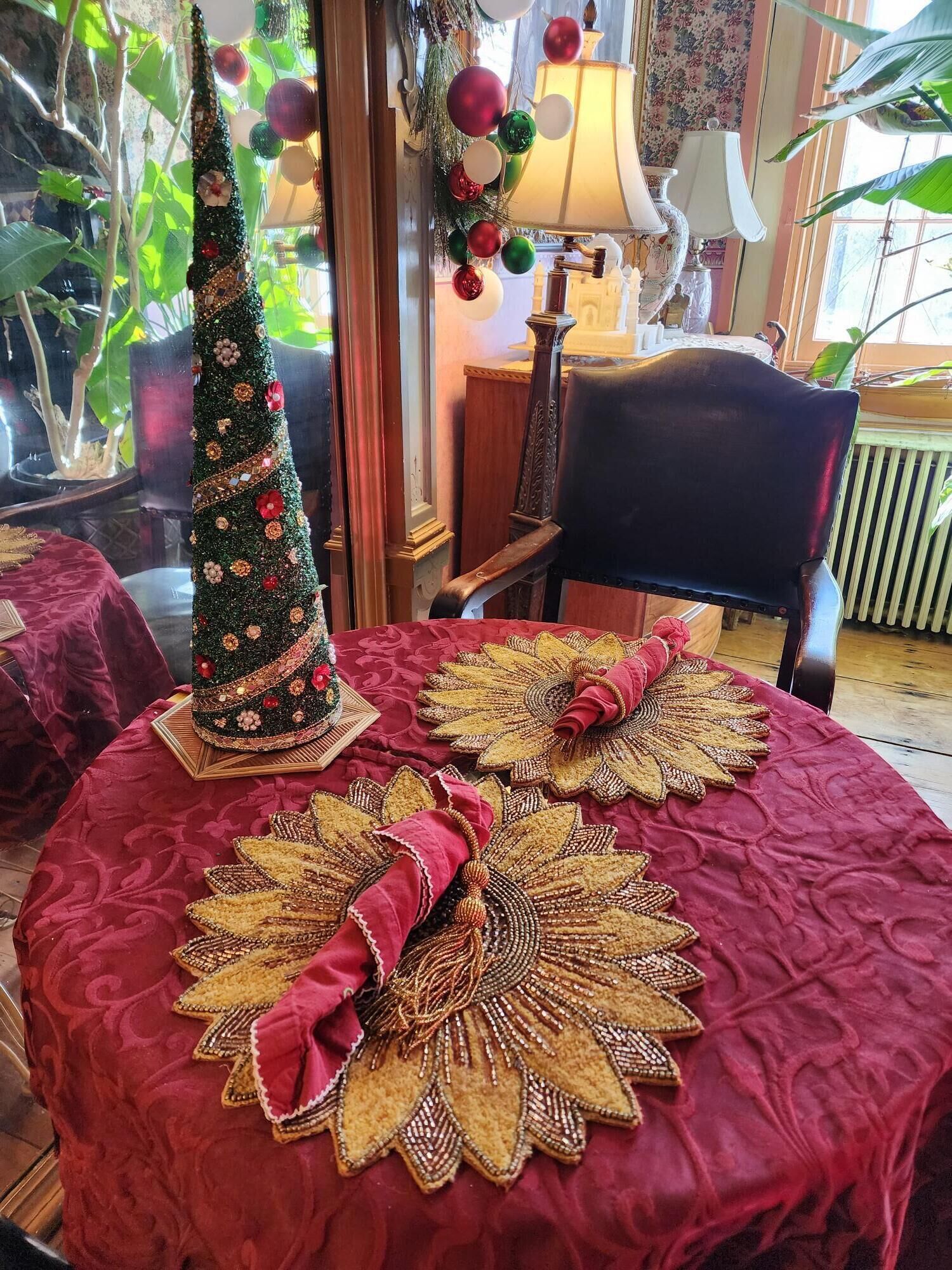 A room with a red upholstered table, a Christmas tree, and decorative tablecloths.