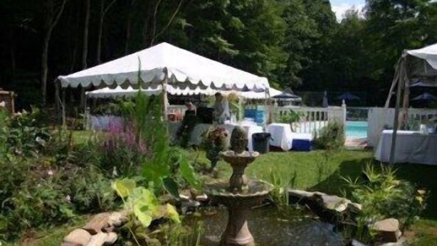 Un jardin avec un étang, une fontaine et une tente blanche.