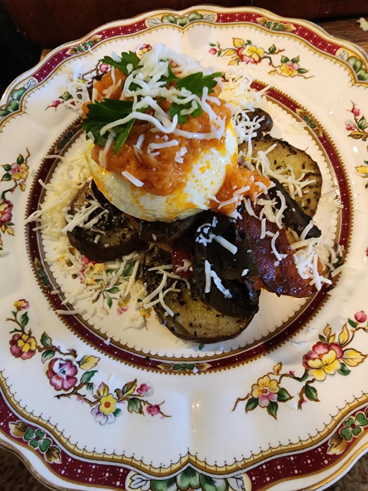 A plate with a decorative floral pattern and a variety of food items including a poached egg, grilled vegetables, and cheese.