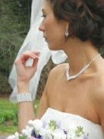 Una persona con un vestido blanco y un ramo de flores, de pie al aire libre con follaje en el fondo.